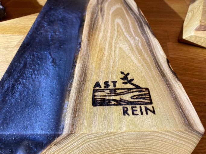 Holzplatte mit eingraviertem Logo "AST REIN" und naturbelassener Oberfläche mit Epoxidharzmittelstreifen.
