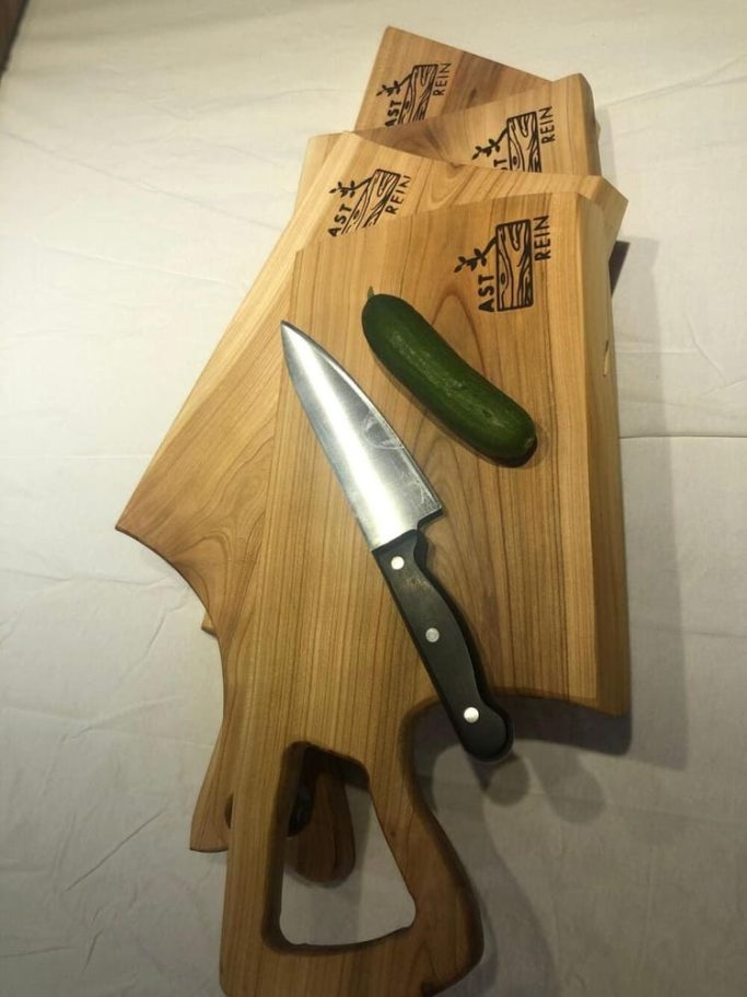 Ein rustikales Holzschneidebrett mit einem Küchenmesser und einer Gurke.