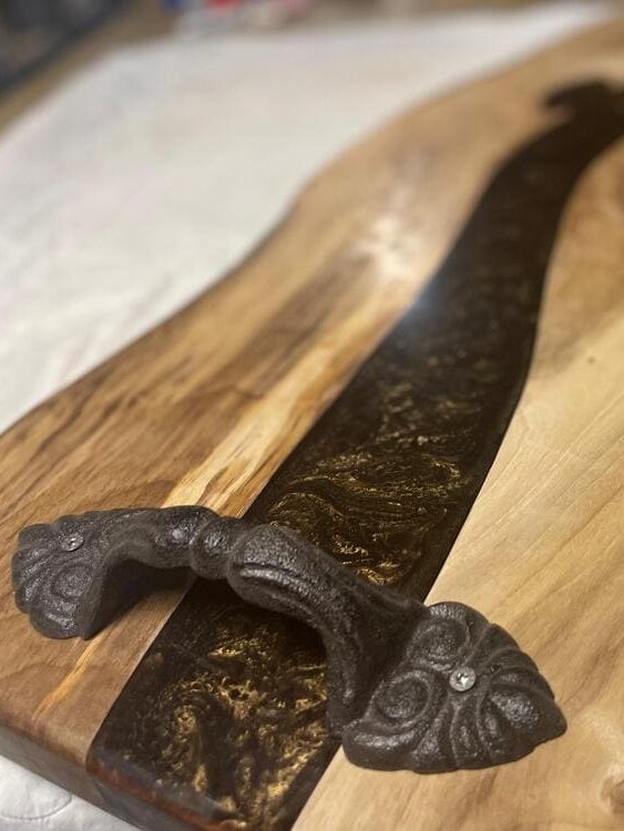 Holzbrett mit Epoxidharz Einlage und dekorativem Metallgriff.