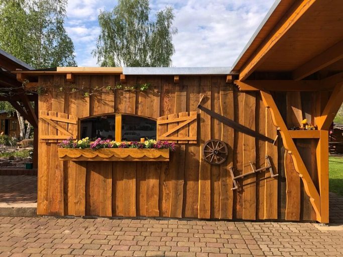 Holzschuppen mit Fenster, Blumenkasten und Holzverzierungen, eingebettet in eine grüne Umgebung.