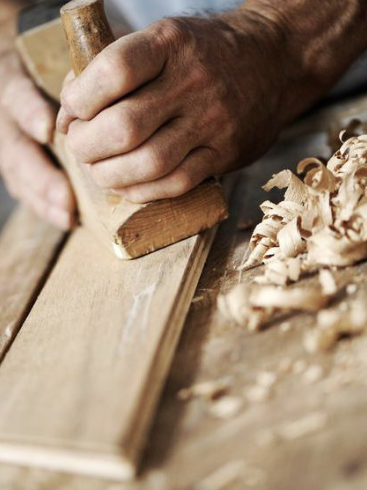 Hände, die mit einem Hobel Holz bearbeiten, um eine glatte Oberfläche zu erzielen.
