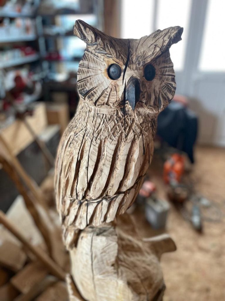 Geschnitzte Holzskulptur einer Eule mit detaillierten Federn und großen Augen.